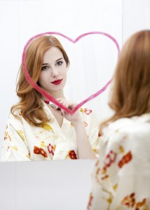 Redhead girl near mirror with heart it in bathroom.